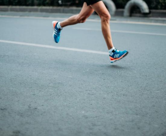 Coureur aux jambes nues et aux chaussures de course bleues claires courant sur une route asphaltée illustrant l'analyse du mouvement de la pression plantaire lors d'exercices de course
