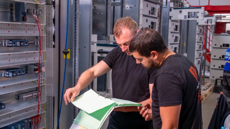 P&V Panels engineer and panel builder reviewing technical documentation beside an electrical control cabinet.