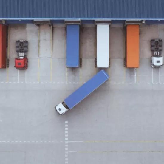Aerial view of trucks and trailers parked at loading bays outside a large warehouse.