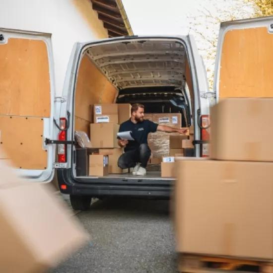 Workers loading cardboard boxes into a delivery van for order dispatch.
