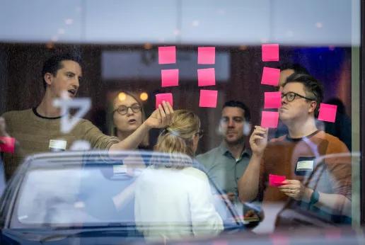People in a brainstorm, looking at post-its on a window. 