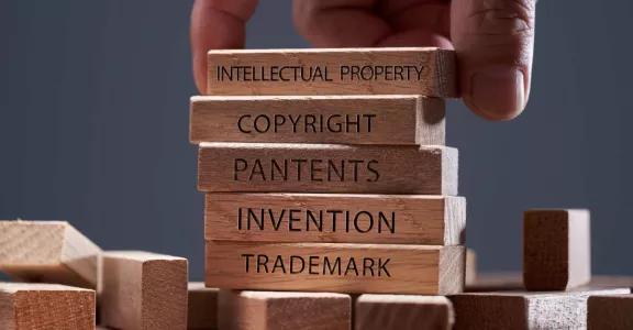 Male hand stacking small wooden blocks labeled intellectual property, copyright, patents, inventions and trademark